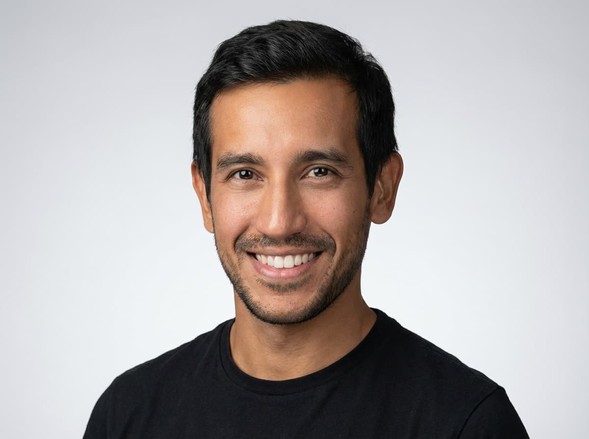 A smiling man with short dark hair and stubble wearing a black t-shirt.
